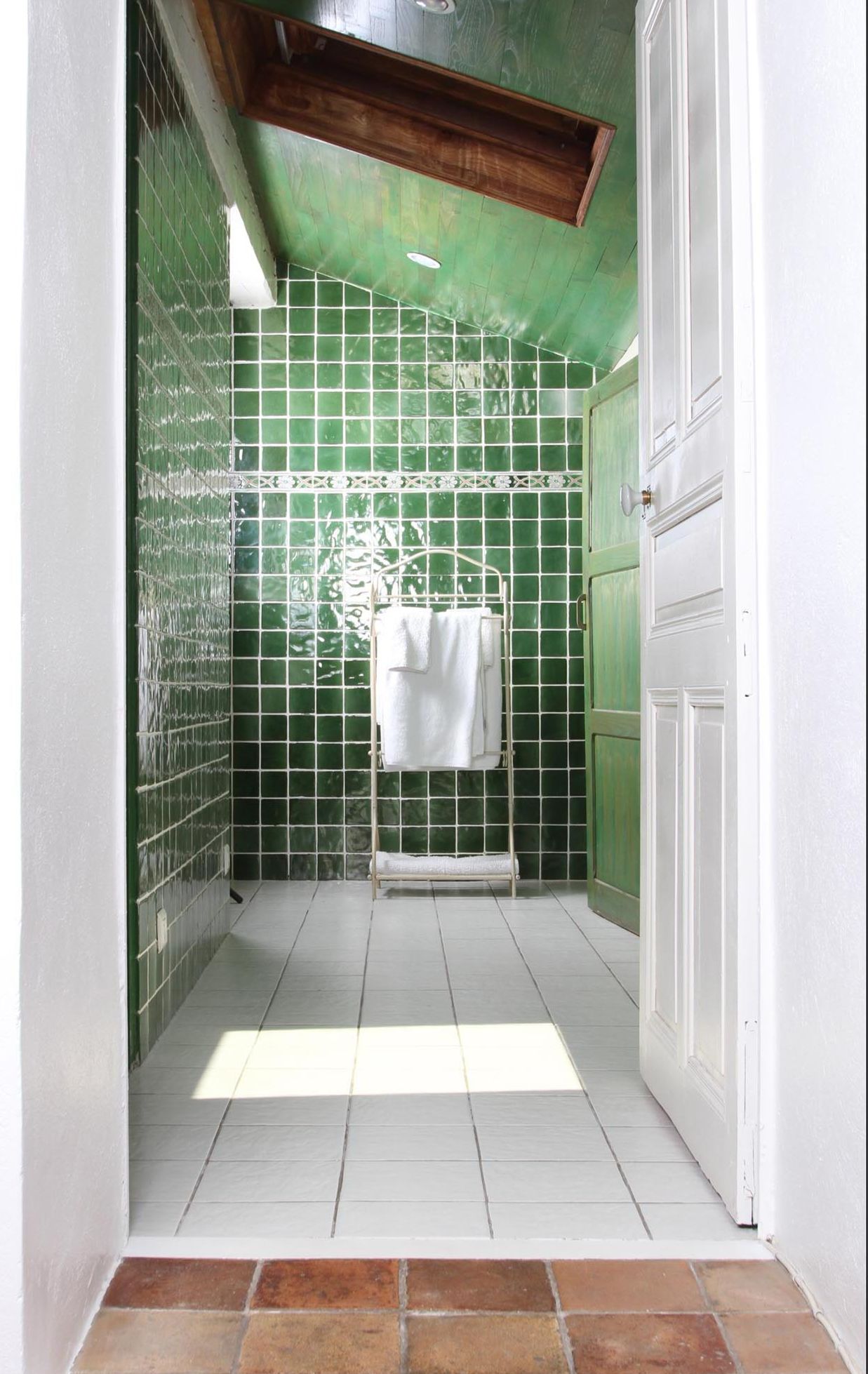 Un baño estrecho con paredes de azulejos verdes, una puerta blanca y suelo de baldosas.
