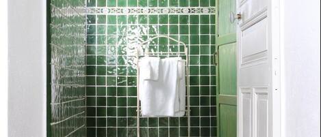 Un baño estrecho con paredes de azulejos verdes, una puerta blanca y suelo de baldosas.