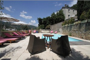 A poolside area with lounge chairs, umbrellas, and a stone wall.