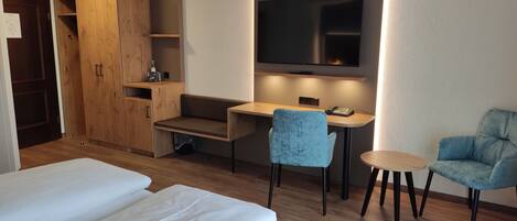 A hotel room with a bed, a desk, a chair, a TV, and a wardrobe.
