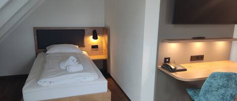 Une chambre à coucher comprenant un lit, une table de chevet, une lampe, un bureau, une chaise et un téléviseur à écran plat.