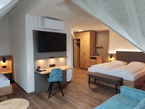 Een moderne hotelkamer met een flatscreen televisie, een bureau met stoel, een bed met een bankje en een houten kledingkast.