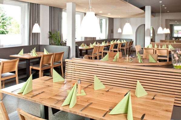 A modern restaurant with wooden tables and chairs, neatly arranged with green napkins and cutlery. - Hotel Restaurant Waldhorn (Friedrichshafen)