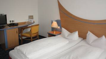 A hotel room with a bed, a desk, a chair, a lamp, and a computer.
