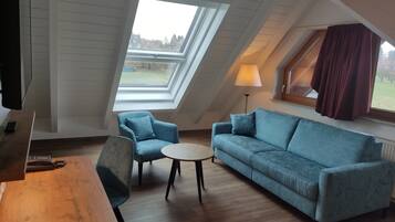 Ein modernes Schlafzimmer im Loft-Stil mit schrägen Wänden, einem Oberlicht und einer gemütlichen Sitzecke mit blauem Sofa und Sesseln.