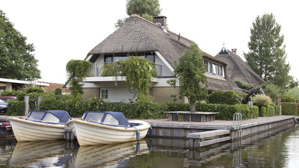 A house with a thatched roof, a balcony, and two boats docked at a pier. - De Mariahoeve (Terherne)