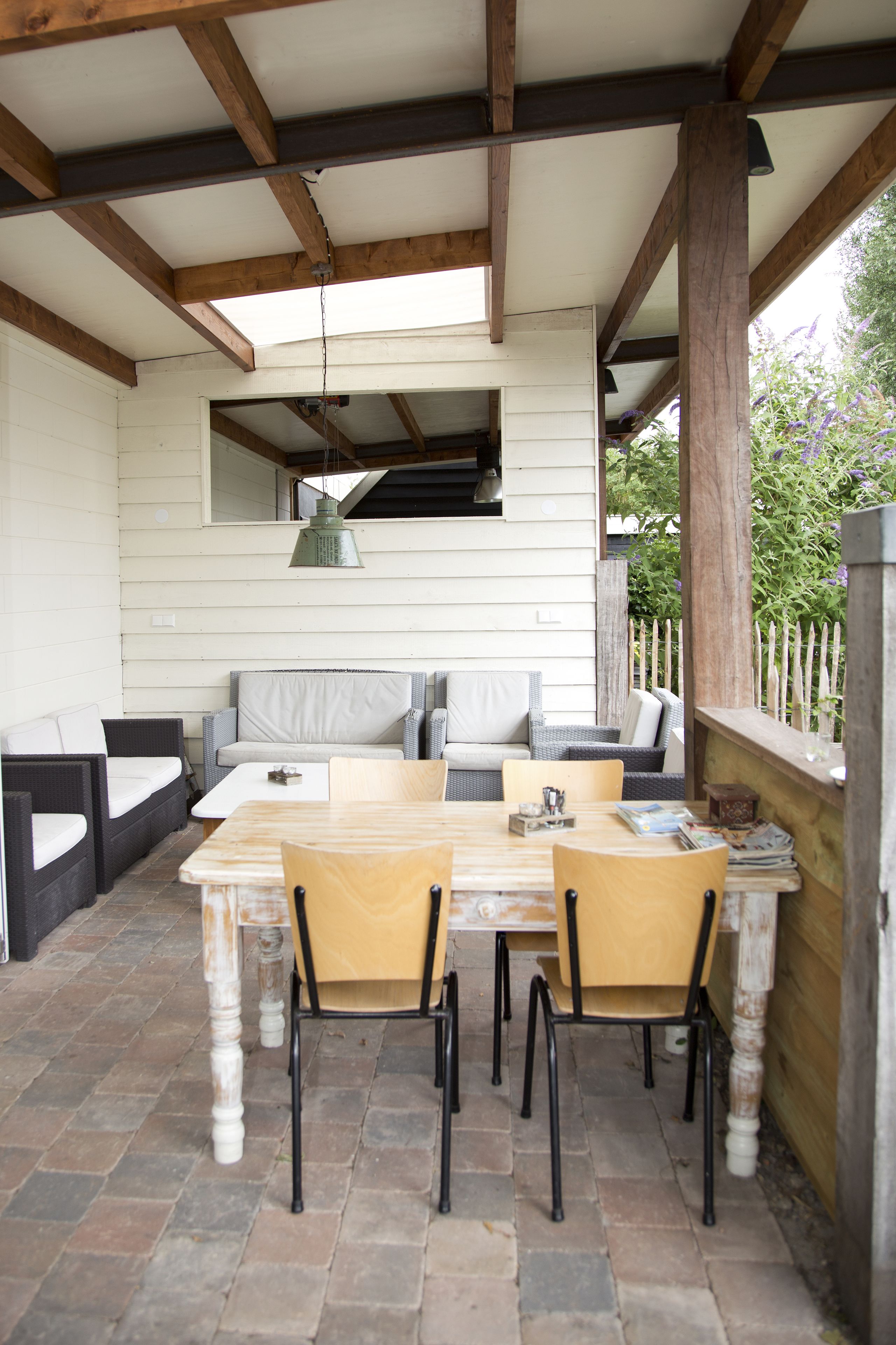 Un patio exterior con una mesa y sillas de madera, un sofá con cojines e ideal, y una lámpara colgante.