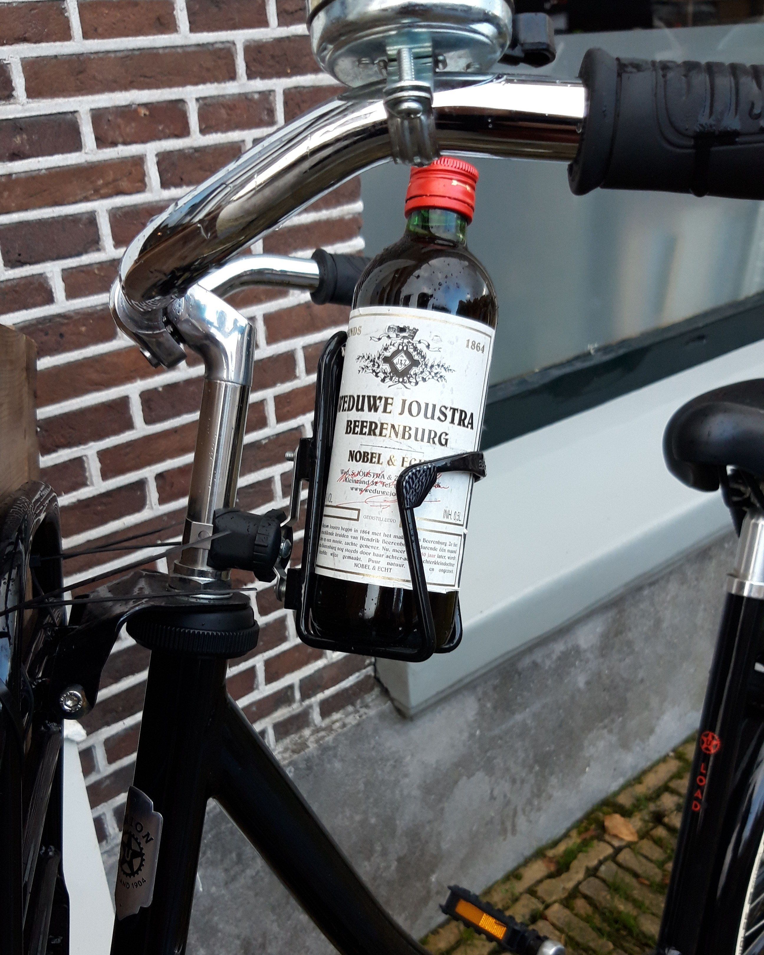 A bottle of beer attached to a bicycle handlebar.