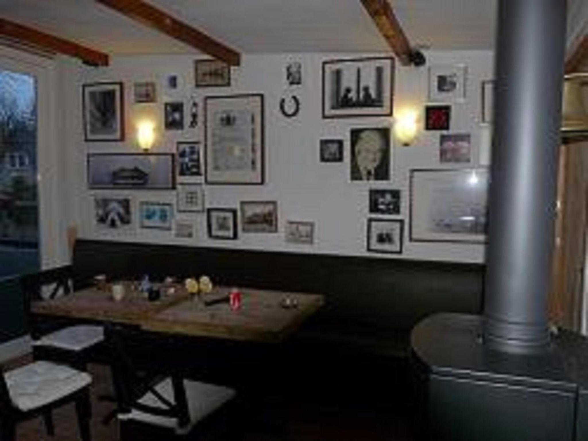 Een kamer met een houten tafel en stoelen, een groot raam en een muur versierd met verschillende ingelijste foto's.