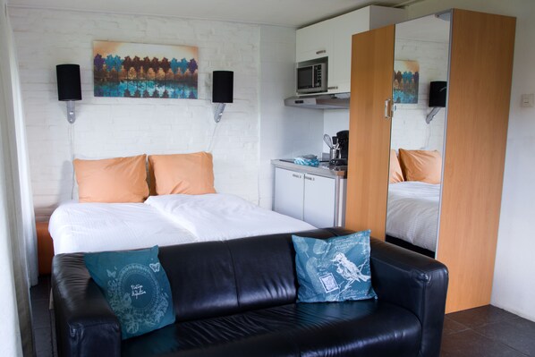 A hotel room with a bed, a black leather sofa, a microwave, and a small kitchenette. - De Mariahoeve (Terherne)