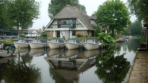 A house with a thatched roof, a dock with several boats, and a calm water body reflecting the surroundings. - De Mariahoeve (Terherne)