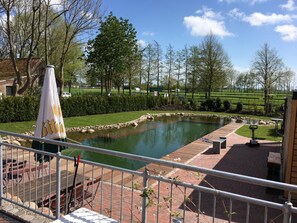 Uitzicht op een vijver met een houten vlonder en zitgedeelte, omringd door bomen en een grasveld.