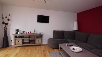 Una sala de estar moderna con un sofá gris, una mesa de centro de madera con un plato de comida, un televisor montado en la pared y un mueble de madera con cestas de almacenamiento.