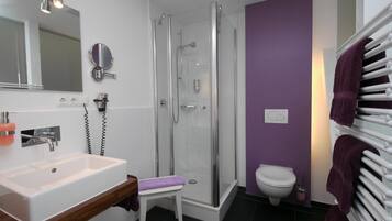 Un baño moderno con ducha envuelta en vidrio, un lavabo blanco y una pared morada.