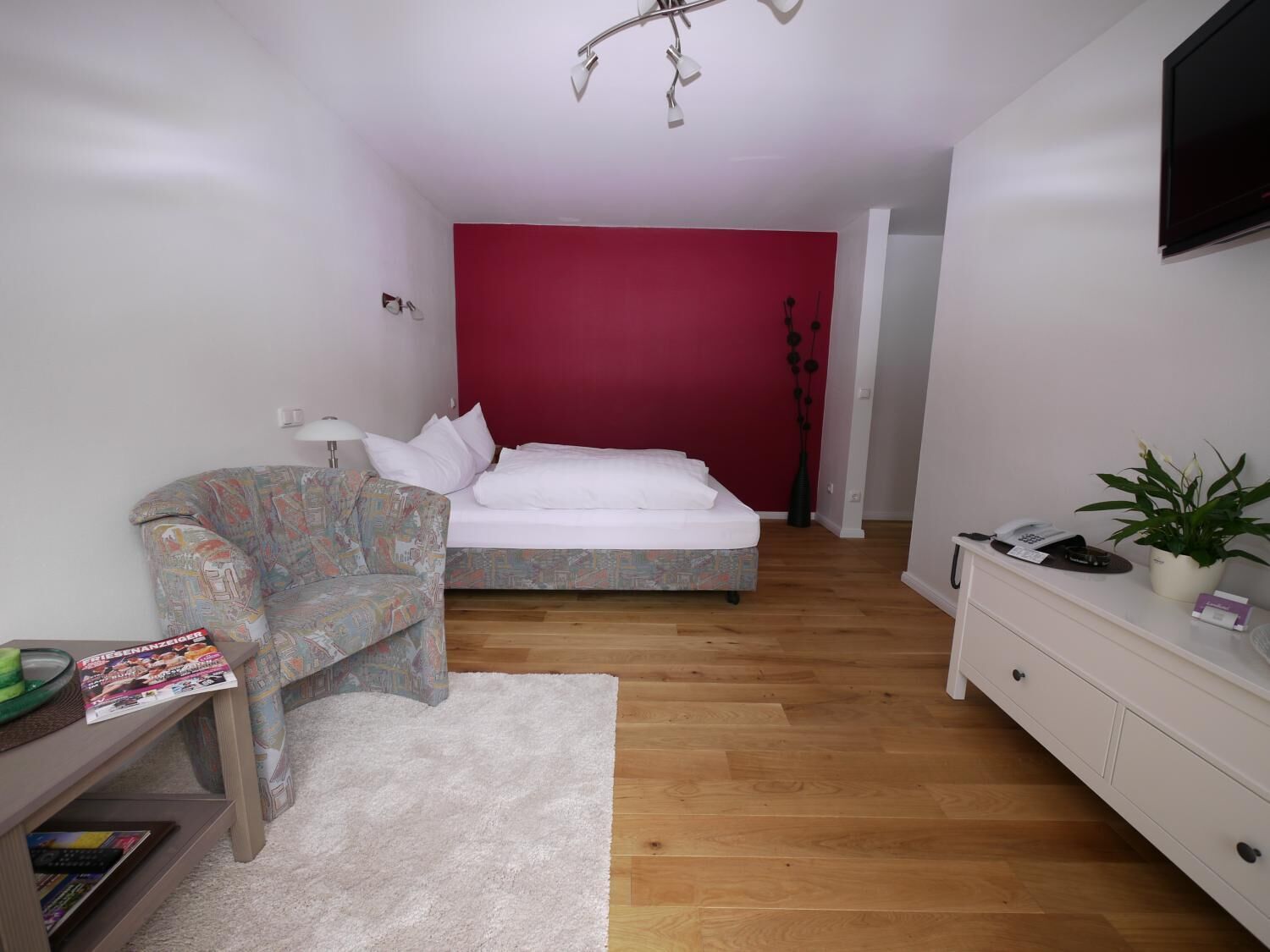 Une chambre à coucher avec un lit, une chaise, un bureau avec une lampe, une commode et une plante en pot.