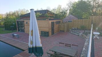 A wooden deck with a pool, a covered seating area, and a stone wall.