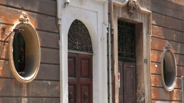 Fachada de edificio con tres ventanas arqueadas y una puerta, cada una con una reja metálica.