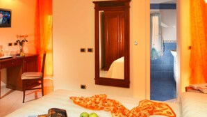 Habitación de hotel con cama, escritorio, silla, espejo y baño visible a través de una puerta abierta.