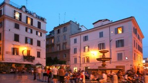 Una plaza pública con una fuente, rodeada de edificios de varios pisos con balcones y ventanas.