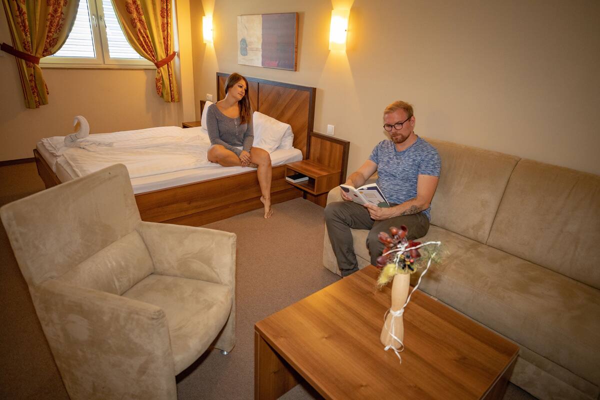 Quarto de hotel com cama, sofá, poltrona e mesa de madeira.
