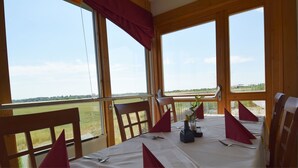 Un comedor con una mesa dispuesta para dos personas, ventanas amplias con vistas a un campo verde y sillas de madera.