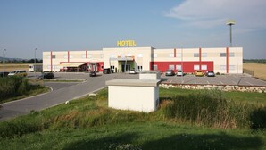 Un hotel con fachada roja y blanca, estacionamiento y cielo despejado.