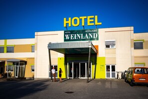 Un hotel con un llamativo letrero que dice 'HOTEL WEINLAND', una entrada cubierta y una furgoneta estacionada.