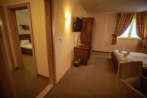 Habitación de hotel con cama, escritorio, silla, televisor y ventana con cortinas.