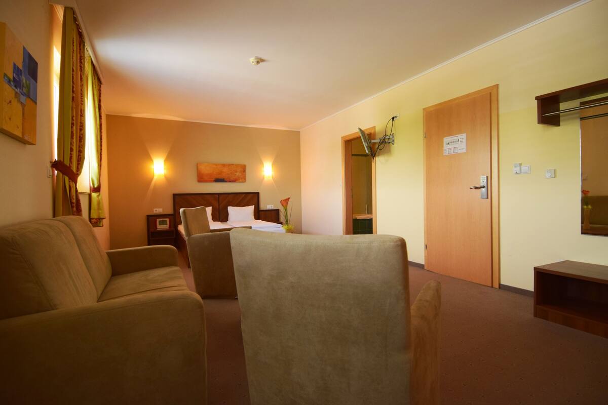 Quarto de hotel com cama, sofá, escrivaninha e espelho.