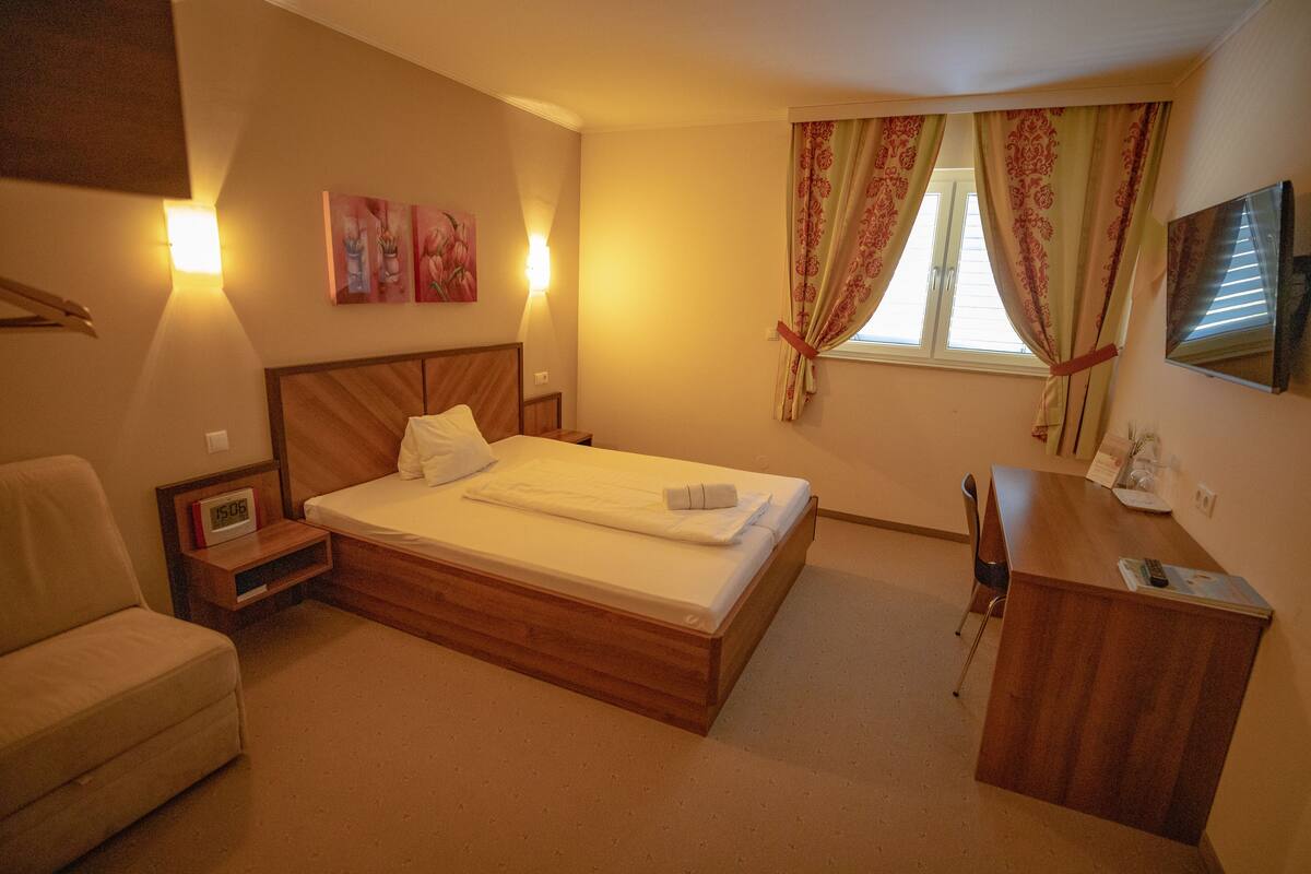 Quarto de hotel com cama, escrivaninha, poltrona, sofá e obras de arte nas paredes.