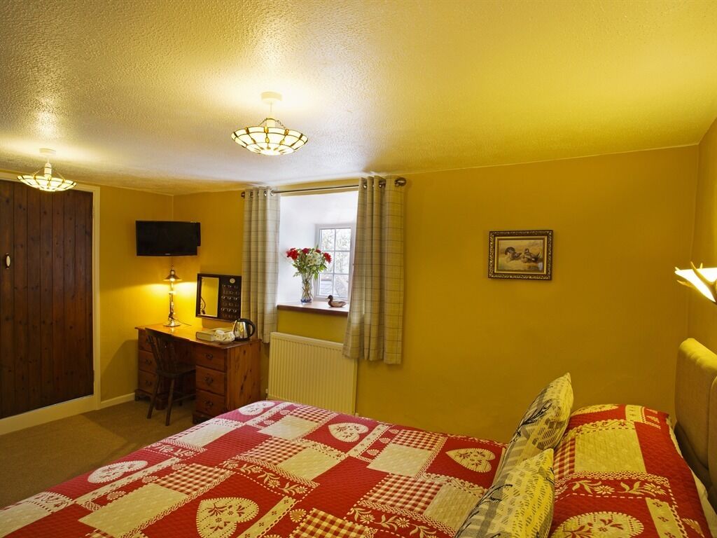 A bedroom with a bed, a desk, a chair, a television, and a window with curtains.