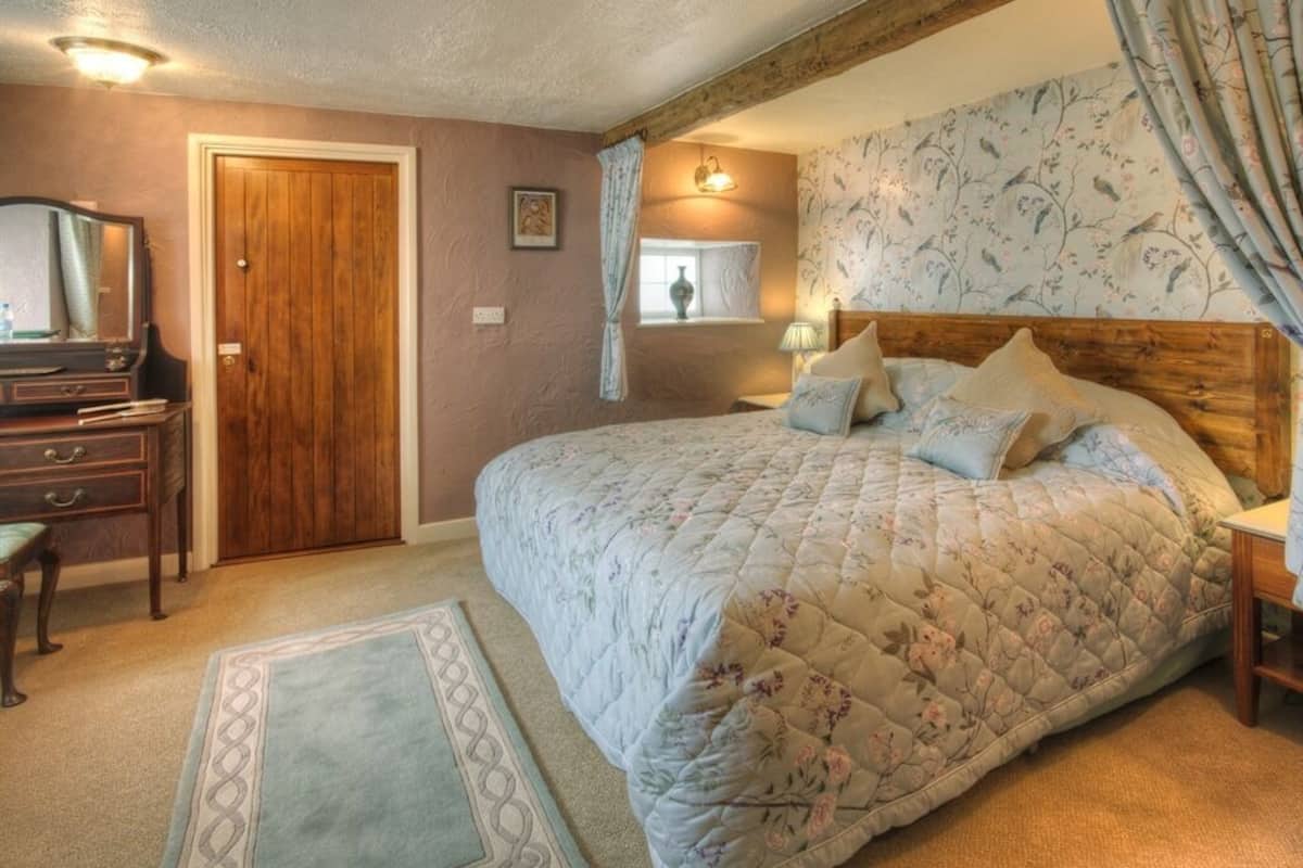 Un dormitorio con una cama grande, cabecera de madera, un aparador, un espejo y una ventana con cortinas.