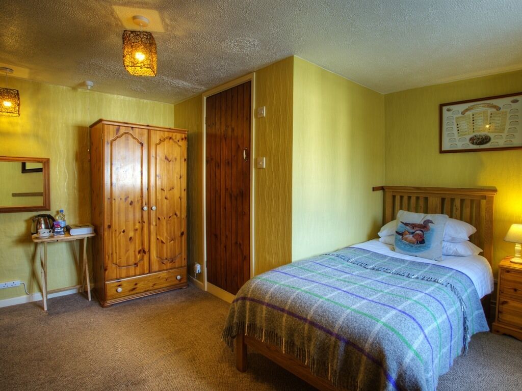 A bedroom with a bed, wooden wardrobe, bedside table, lamp, and a framed picture on the wall.