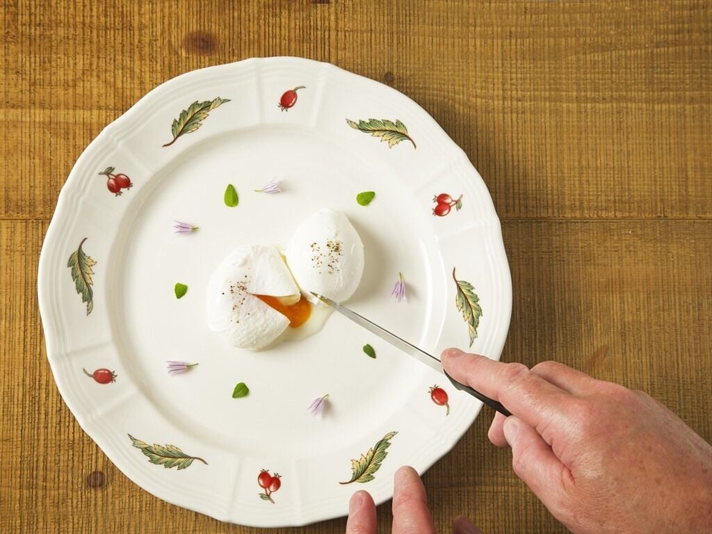 A white plate with red berries and green leaves design, a dollop of cream, and a knife cutting into it.