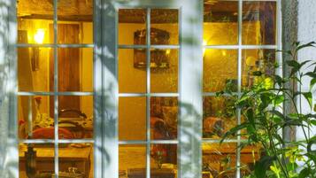 A room with a large window divided into multiple panes, revealing a cozy interior with wooden furniture and a vase with flowers.
