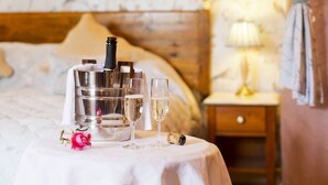 A neatly arranged table with a bottle of champagne, two glasses, and a corkscrew on a bed with a wooden headboard. - Tinhay Mill Guest House (Lifton)