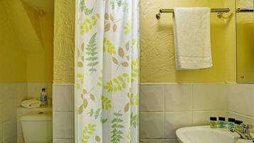 A bathroom with a toilet, sink, and shower curtain with a leaf pattern.