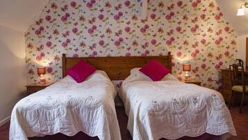 A bedroom with two beds, floral wallpaper, and bedside lamps.