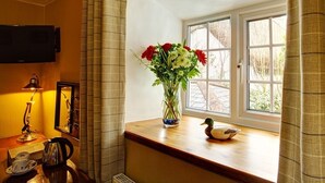 A room with a wooden desk, a vase with flowers, a duck figurine, and a window with curtains. - Tinhay Mill Guest House (Lifton)