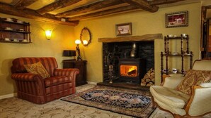 A cozy living room with a fireplace, leather armchair, patterned rug, and wooden furniture. - Tinhay Mill Guest House (Lifton)