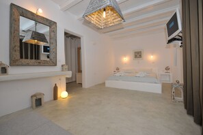 A bedroom with a large bed, a mirror, a television, and a unique ceiling light fixture. - Anemoi Resort (Paros)