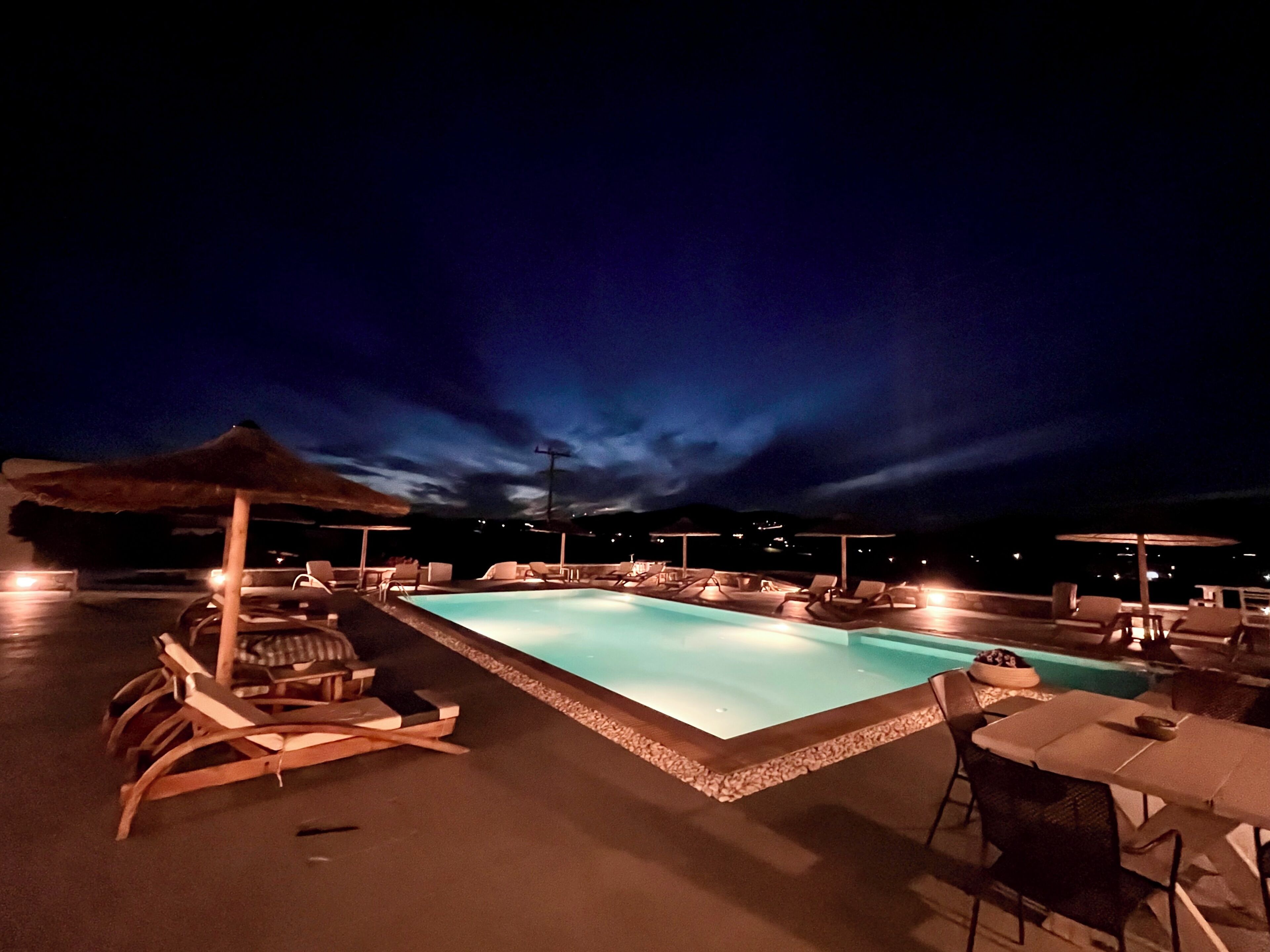 Zona de piscina nocturna con sillones de descanso y sombrillas.