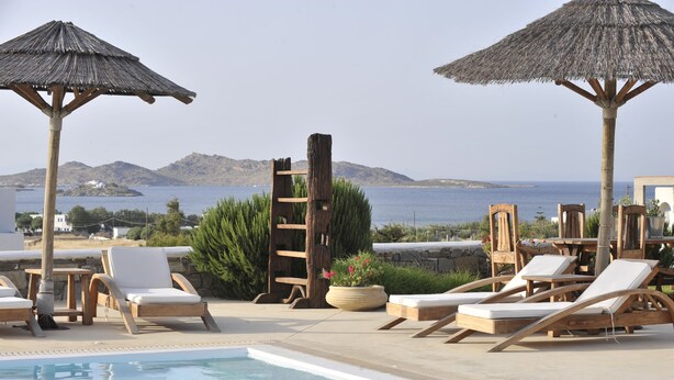 A poolside area with lounge chairs and umbrellas, overlooking a body of water and hills.