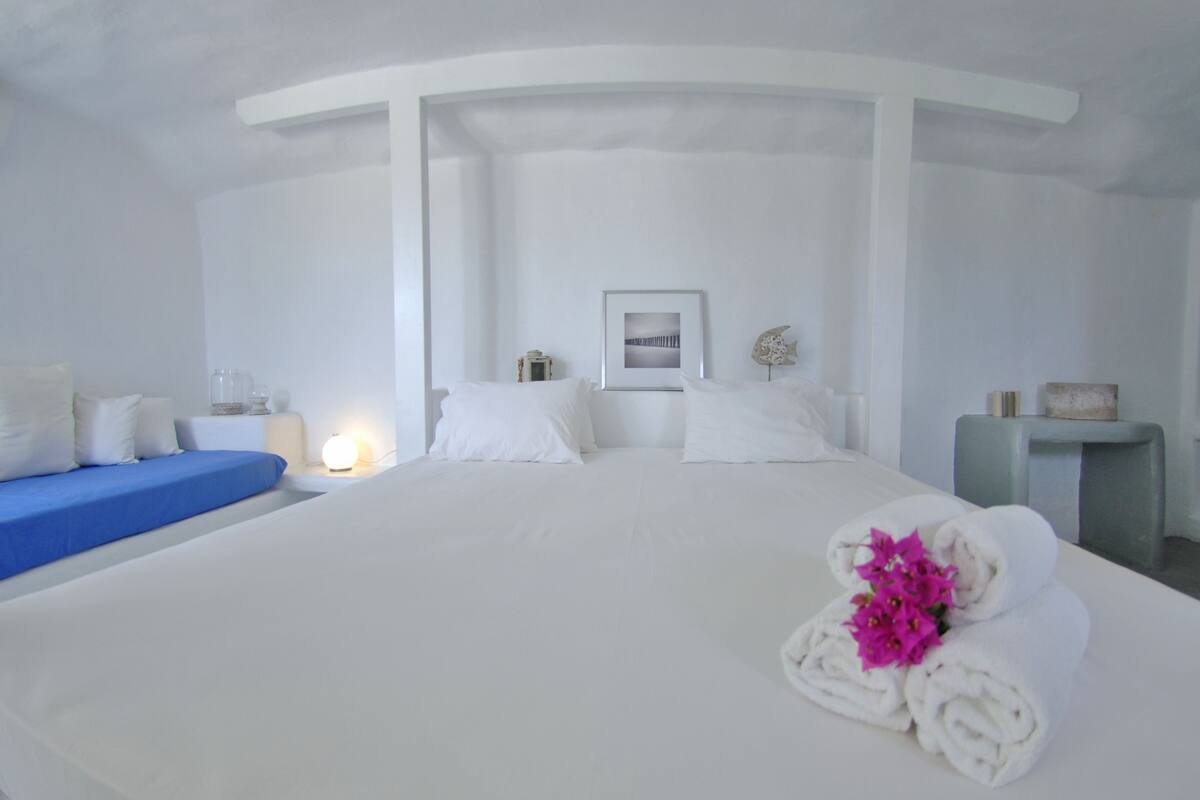 Habitación de hotel con una cama grande, un sofá azul, una mesita de noche con una lámpara y un cuadro en la pared.