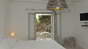 A bedroom with a bed, a table, chairs, a TV, and a view of the outdoors.