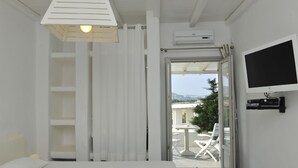 A bedroom with a bed, a TV, an air conditioning unit, and a balcony with chairs.
