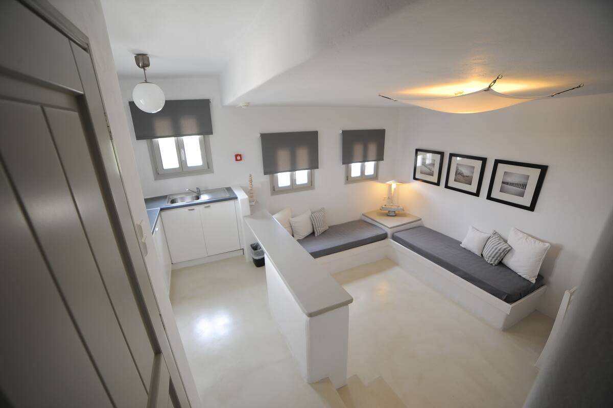 Un espacio habitable compacto con kitchenette, una zona de estar con un banco y una mesa de comedor.