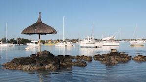 A marina with boats docked, a thatched umbrella, and rocky outcrops in the water. - Auberge Miko (Grand-Baie)