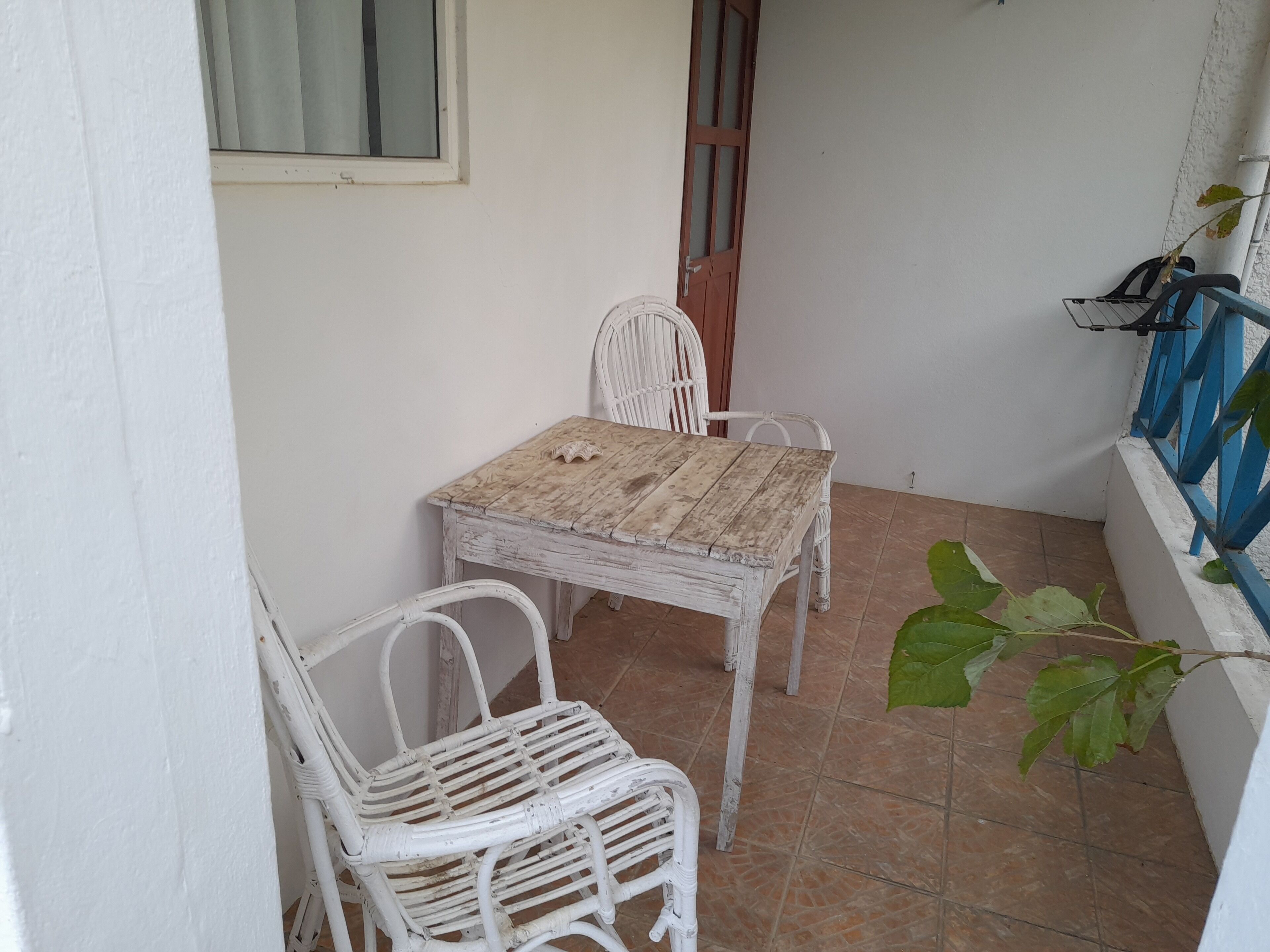 Un pequeño patio con una mesa de madera rústica y sillas de mimbre blanco.