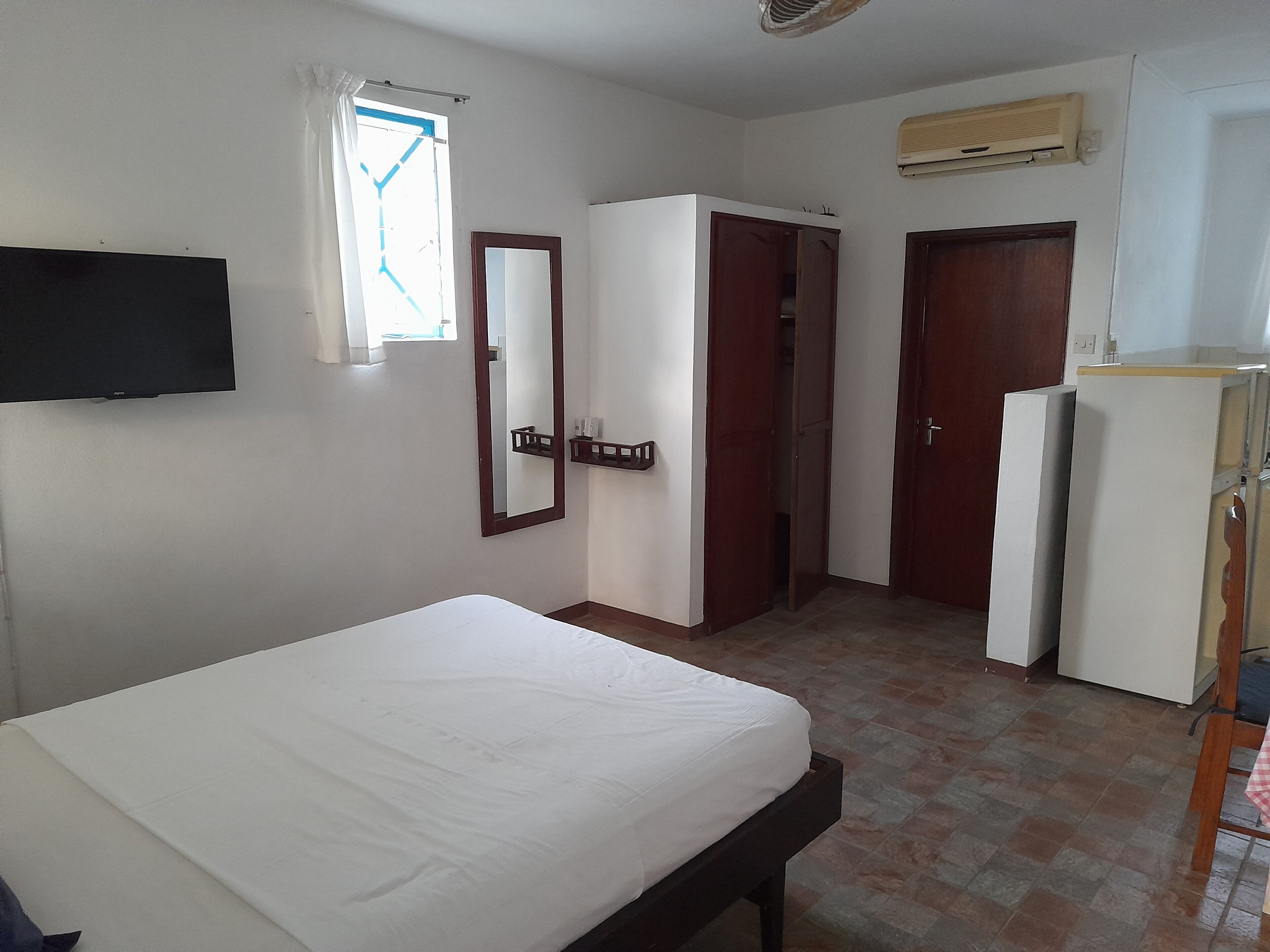 A room with a bed, a wardrobe, a mirror, a door, and an air conditioning unit.